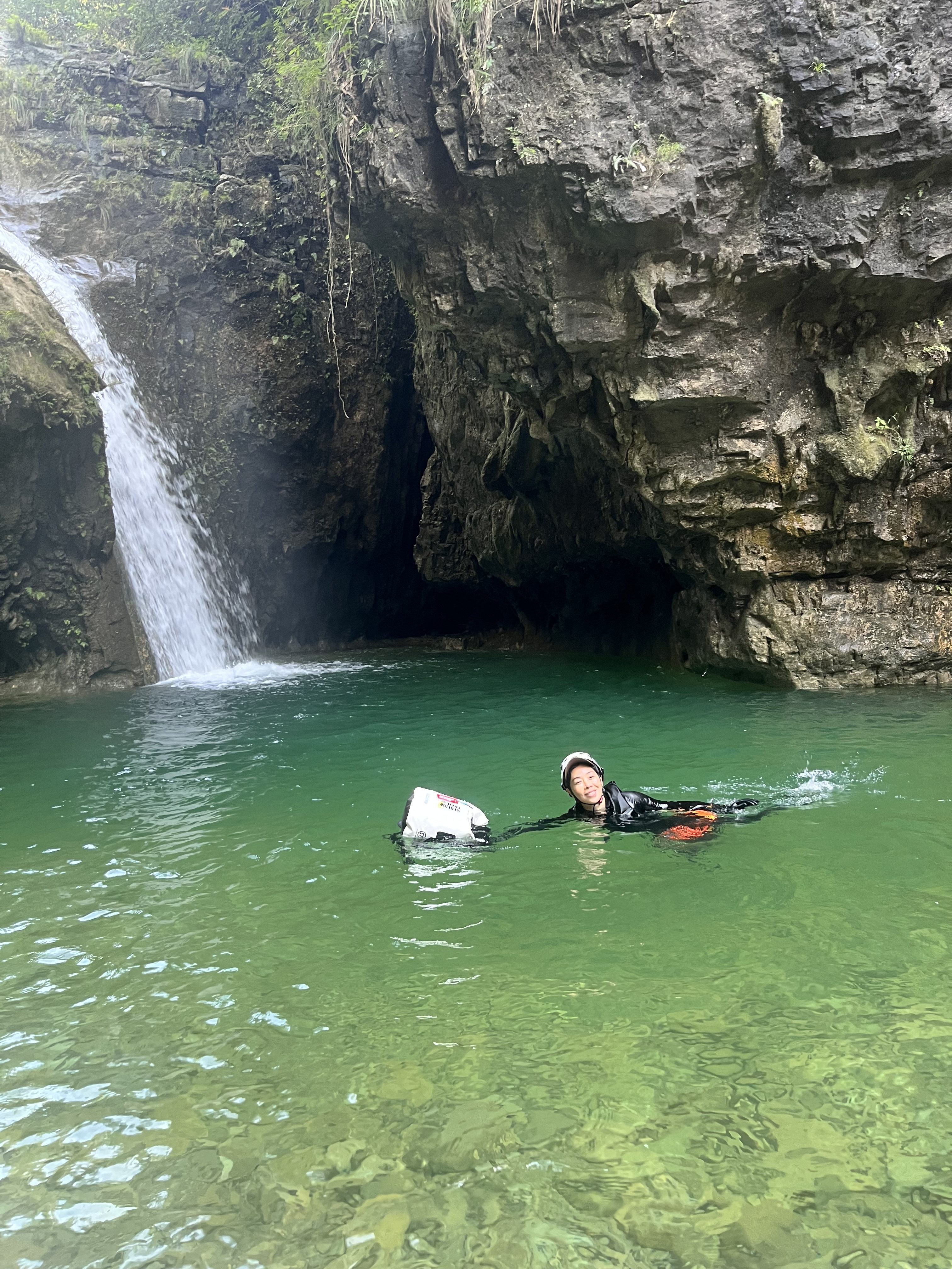 A person swimming through a deep pool in a canyon with a waterfall in the background.