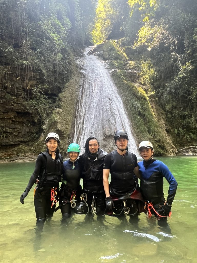 A portrait of five people below a waterfall on a canyoning tour.