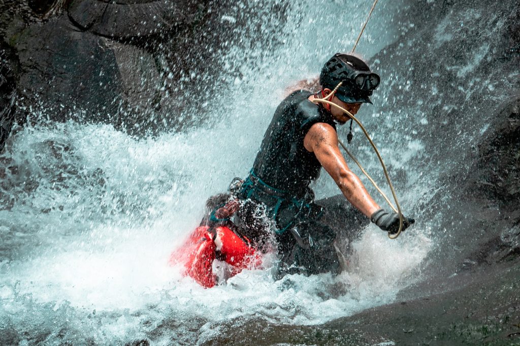 A canyoning guide quickly descending into a pool of water.