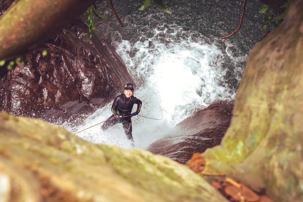 a client on canyoning tour smiling as he rappels down a waterfall 
