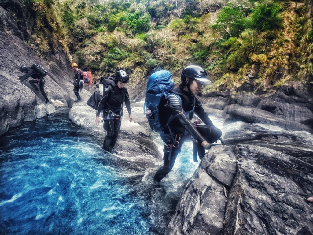 A group of people walks through a river and over boulders.