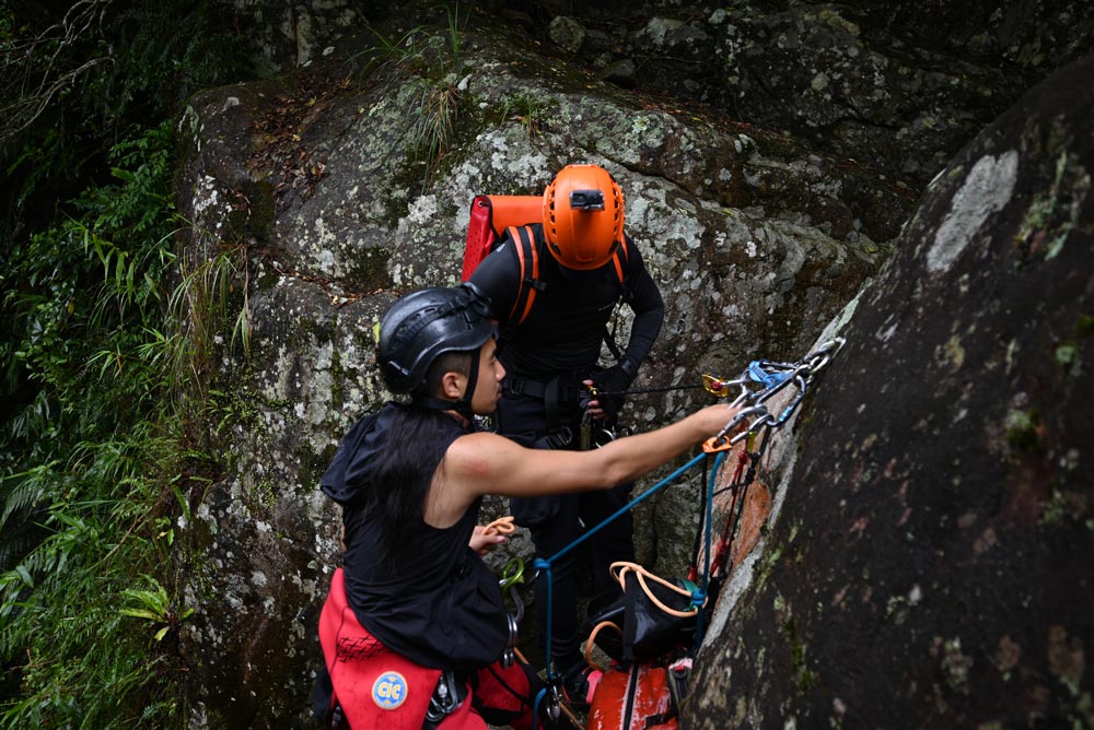 Canyoning guide instructs client at a rappel station.